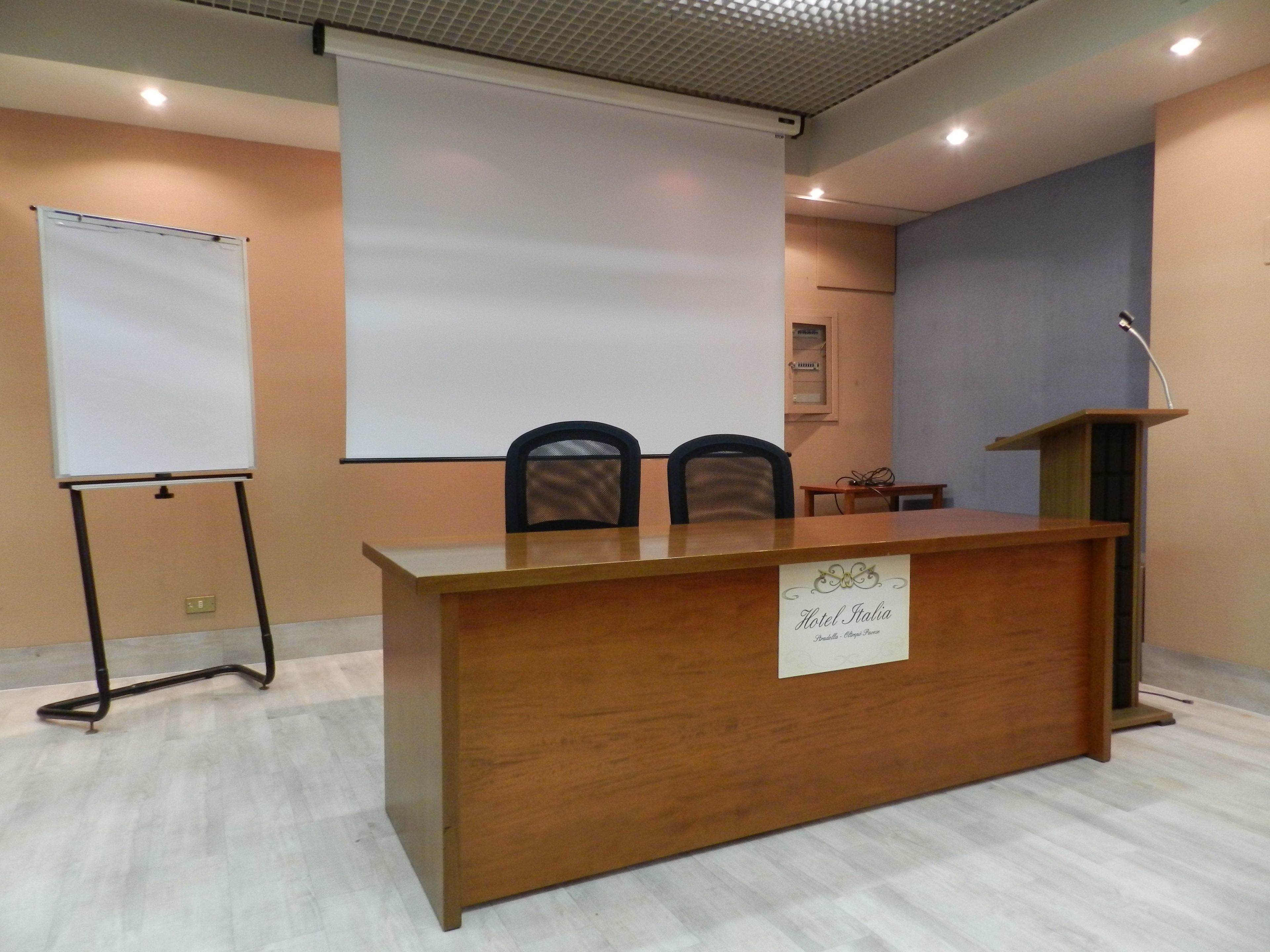 A conference room with a wooden desk, two chairs, a projector screen, and a podium.