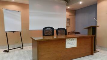 A conference room with a wooden desk, two chairs, a projector screen, and a podium.