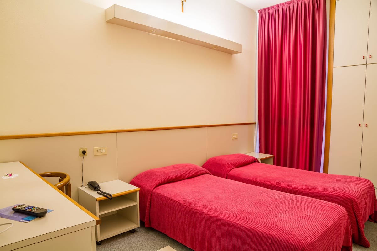 Habitación de hotel con dos camas individuales, un escritorio con teléfono y un armario.