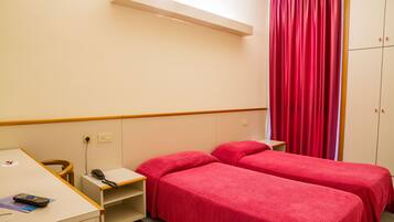 A hotel room with two single beds, a desk with a telephone, and a wardrobe.