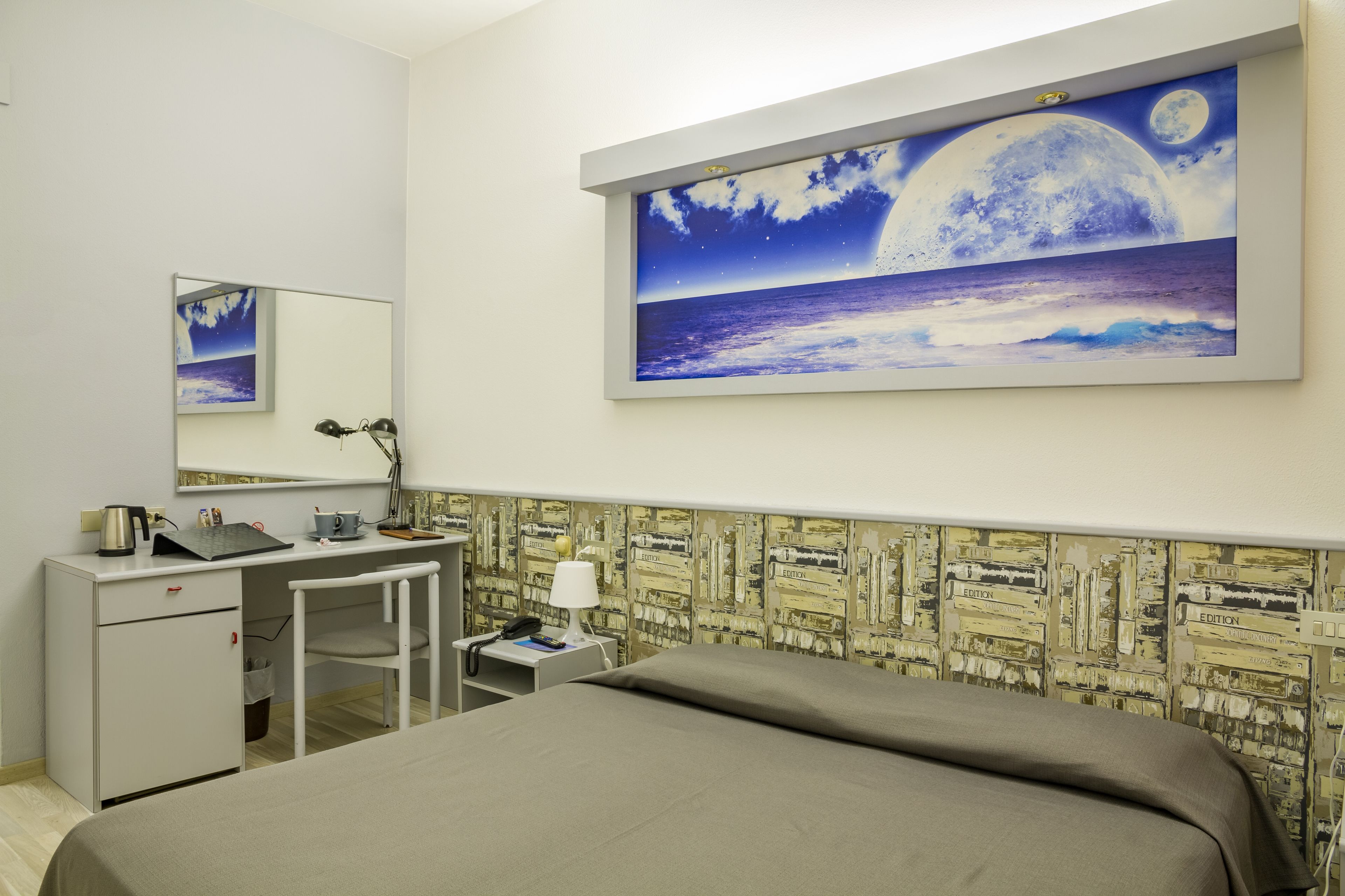 Une chambre d’hôtel avec un lit, un bureau, une chaise et un grand tableau représentant une mer illuminée par la lune.