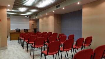 A conference room with rows of red chairs, a podium, and a projector screen.