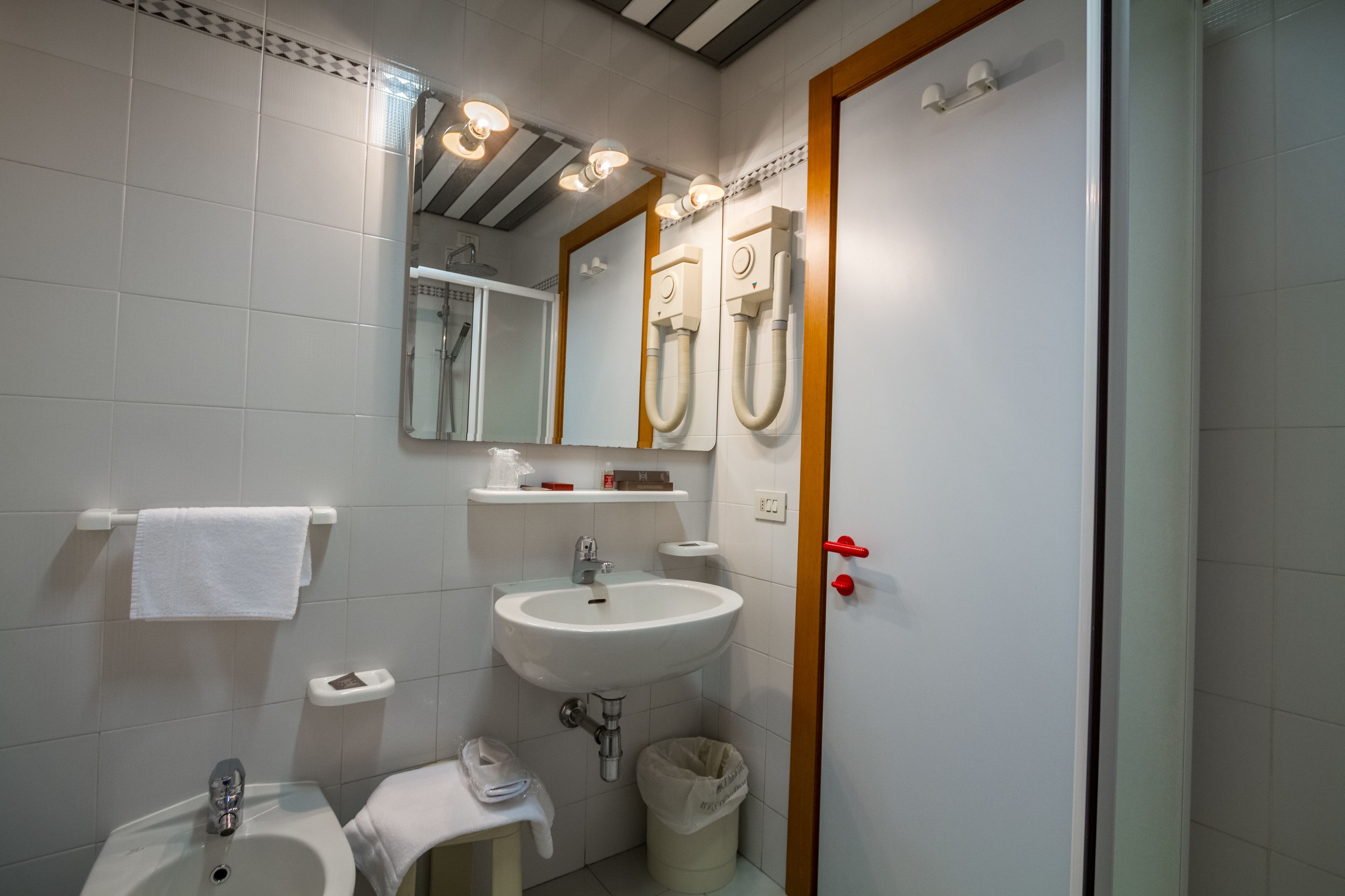 Un bagno con lavandino, specchio, porta asciugamani e una porta con maniglia rossa.