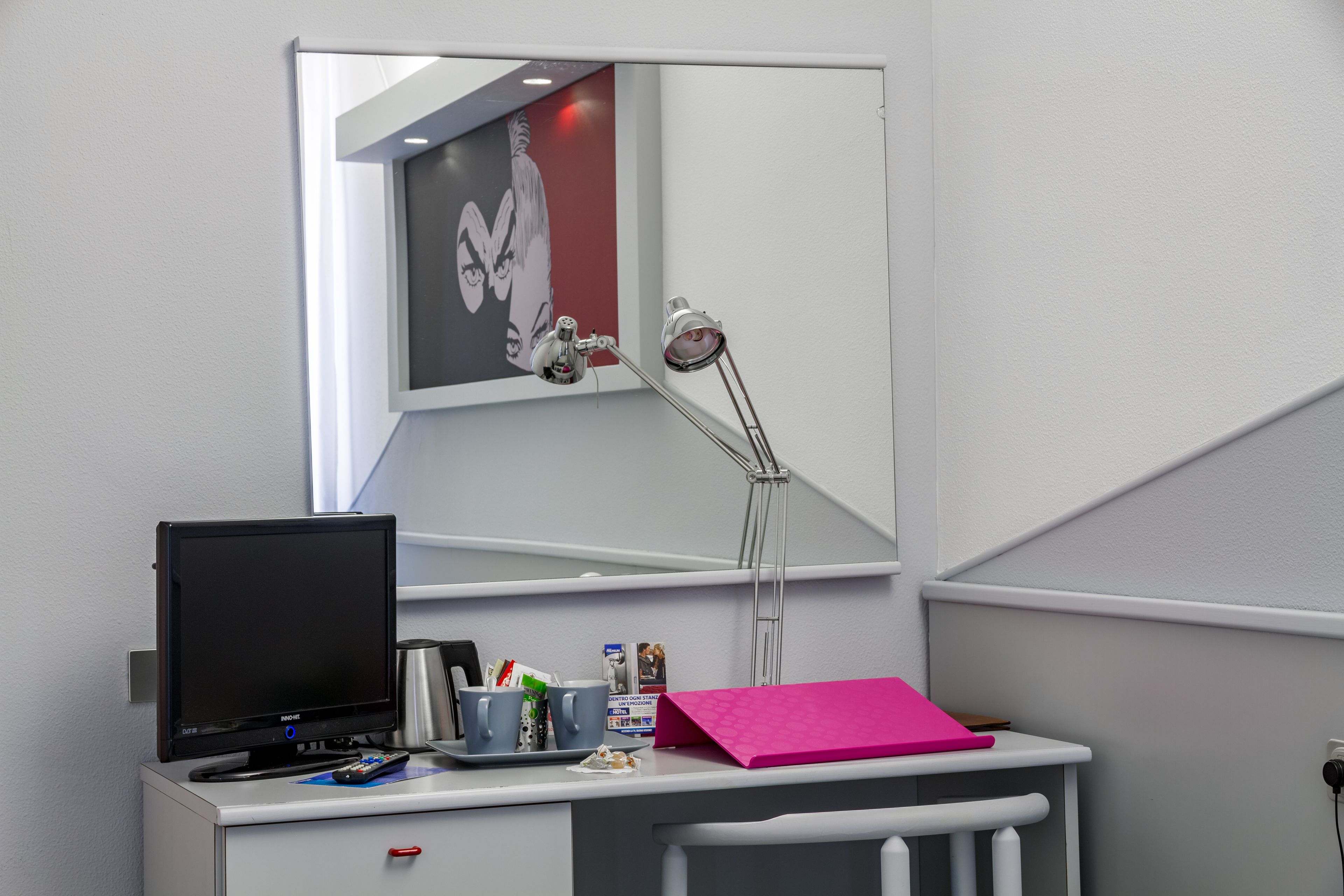 A desk with a computer, a mirror, a lamp, and various items on the desk.