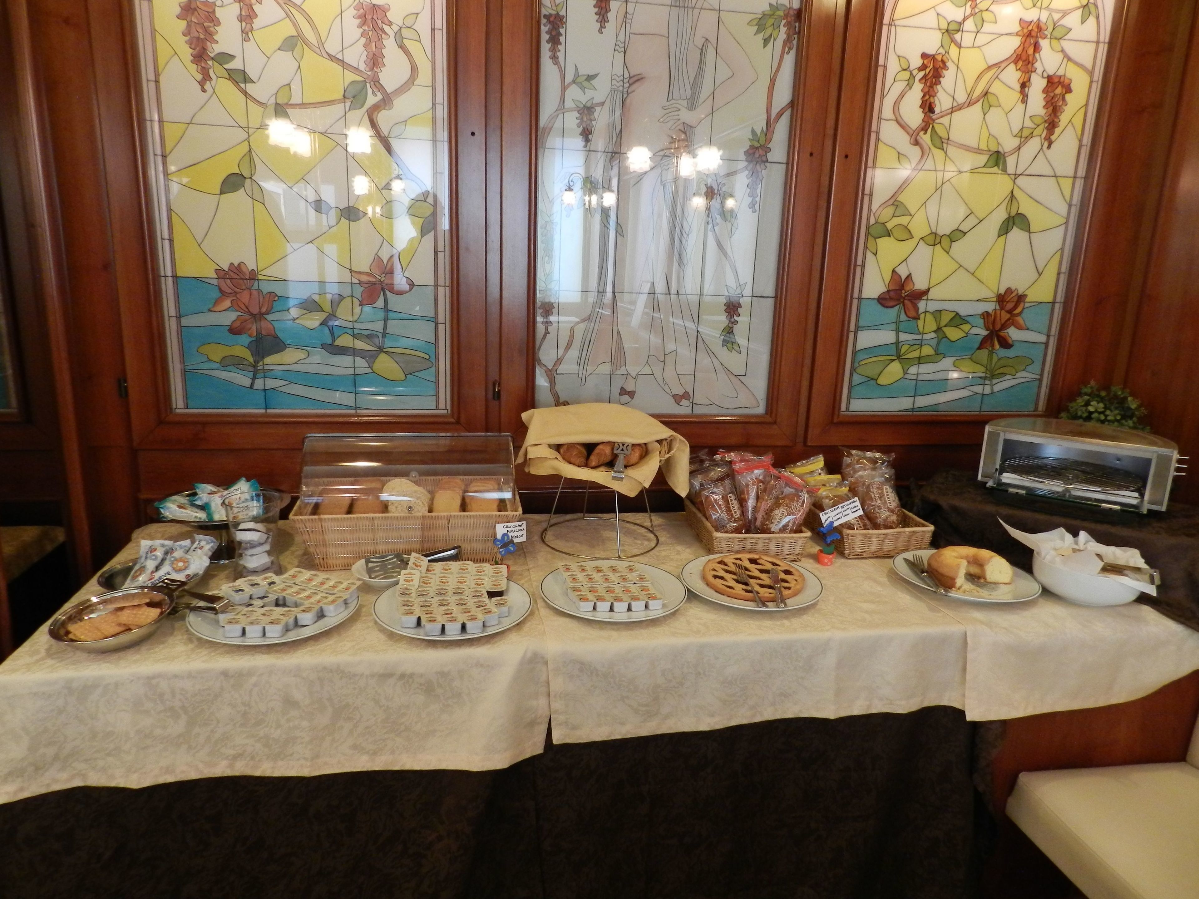 A breakfast buffet with various pastries, bread, and baked goods displayed on a table with a tablecloth.