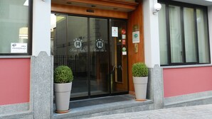 A hotel entrance with a sign reading "HOTEL ISTORIA," featuring a glass door, potted plants, and various certifications on the wall. - Hotel Italia (Stradella)