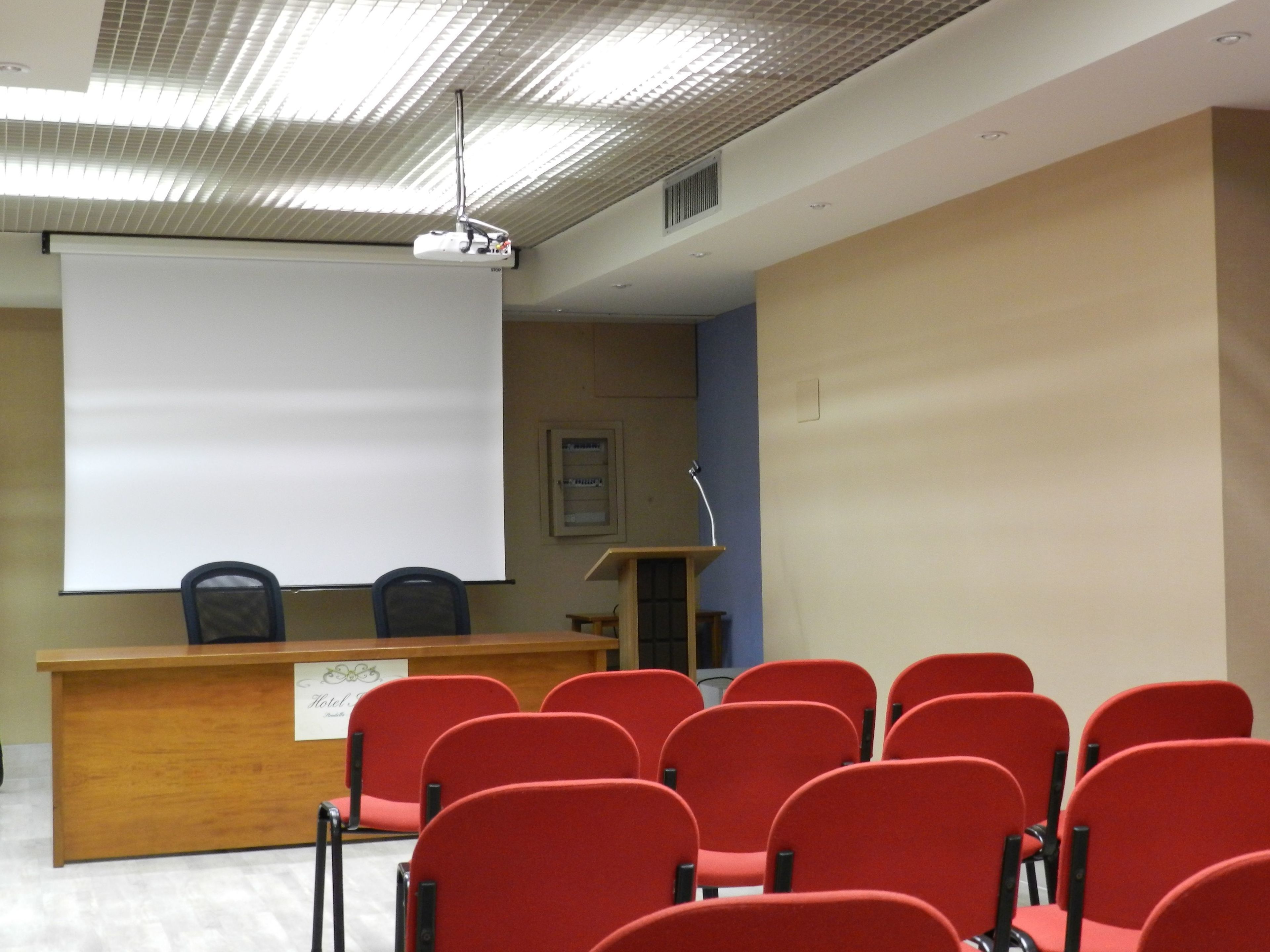 A conference room with a podium, a whiteboard, and red chairs.