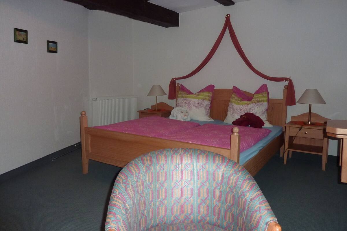 Un dormitorio con una cama de madera, dos mesitas de noche, una silla y un dosel rojo sobre la cama.