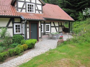 A traditional half-timbered house with a red-tiled roof, a front door, and a small outdoor seating area with a table and chairs. - Hof Guttels (Rotenburg an der Fulda)