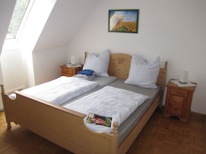 A twin bed with a wooden headboard, two bedside tables, a nightstand, a window, and a painting on the wall. - Hof Guttels (Rotenburg an der Fulda)