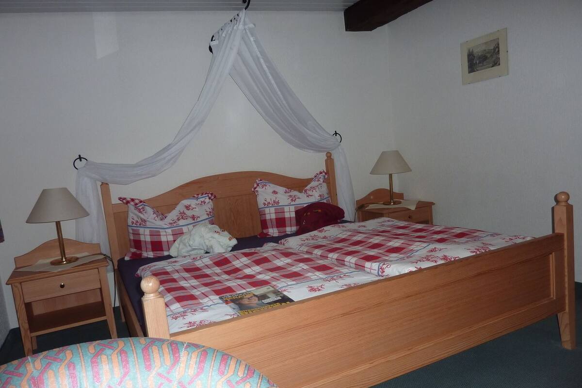 Un dormitorio con una cama de madera, dos mesitas de noche con lámparas, una mesita auxiliar y un dosel.
