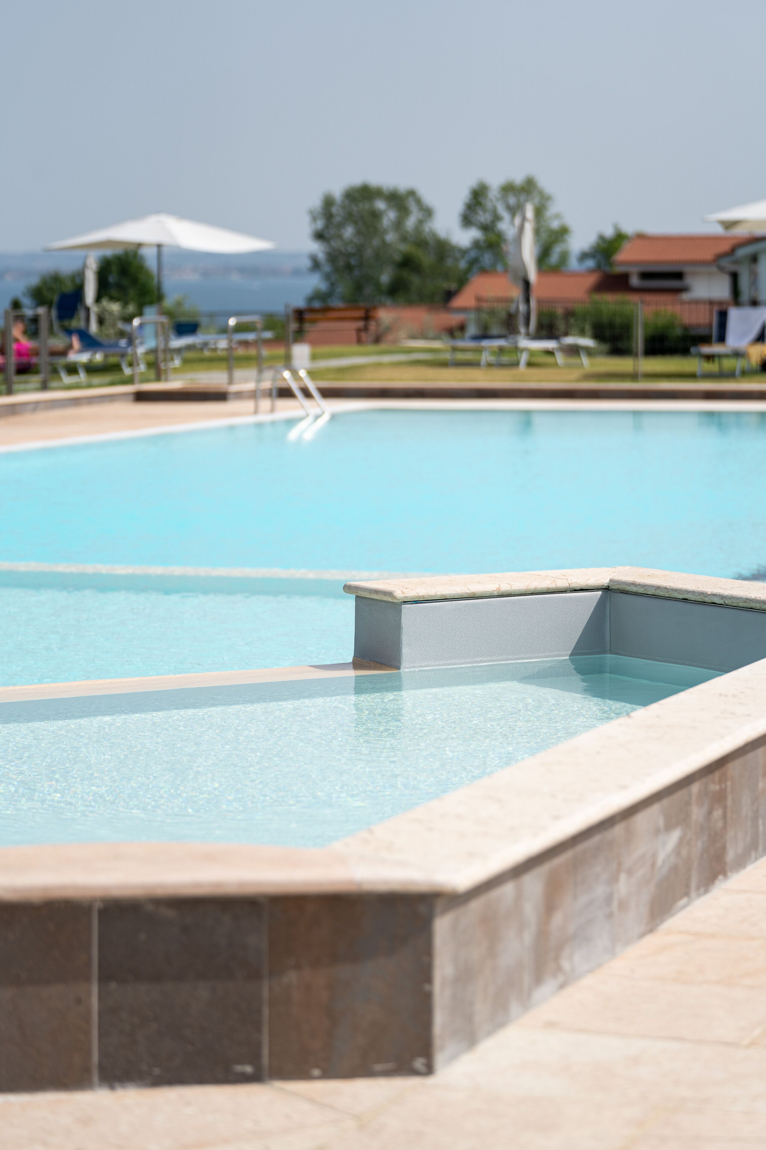 Ein Swimmingpool mit klarem, blauem Wasser, umgeben von Liegestühlen und Sonnenschirmen.