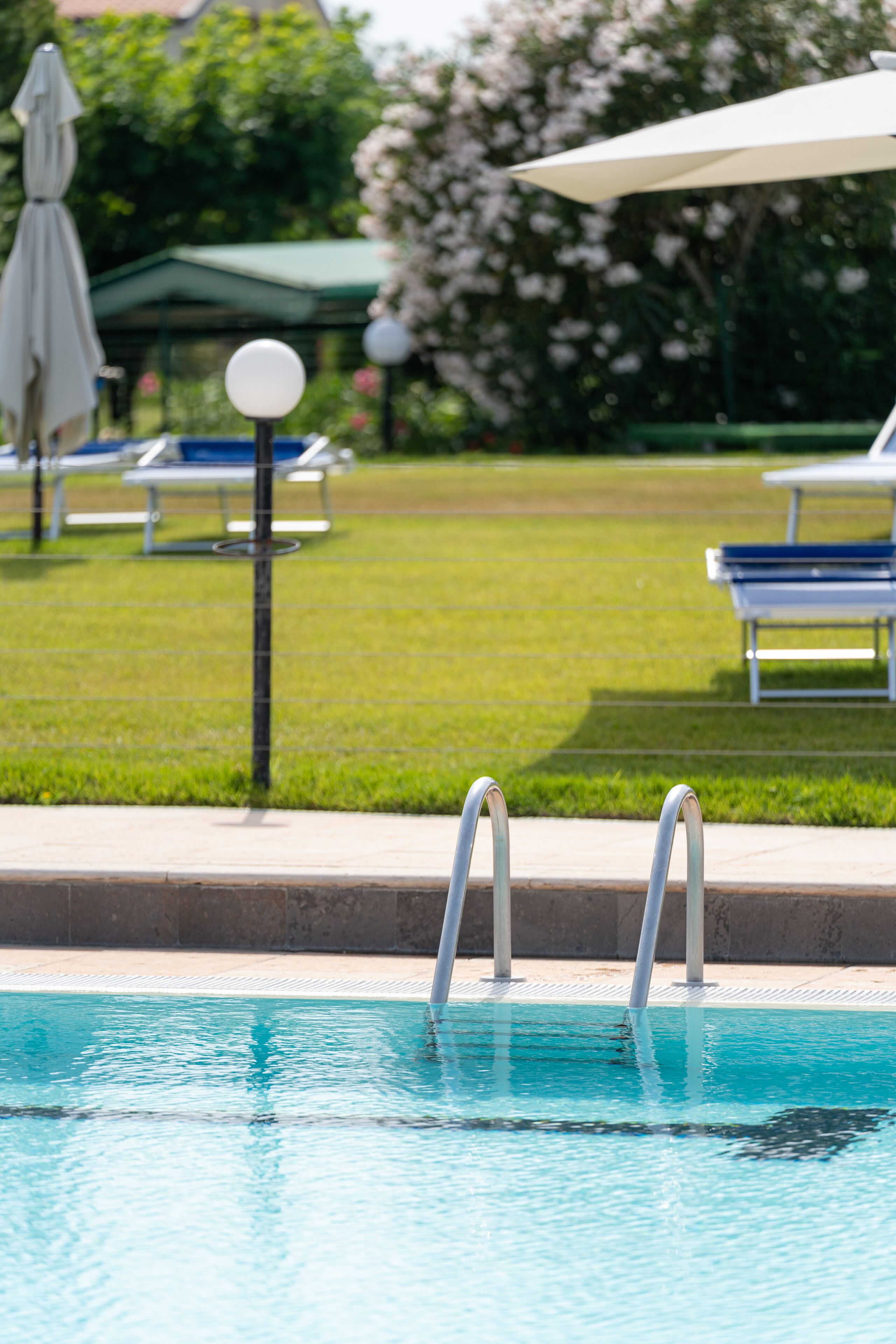 A swimming pool with metal ladders, a grassy area with lounge chairs, and a white umbrella.