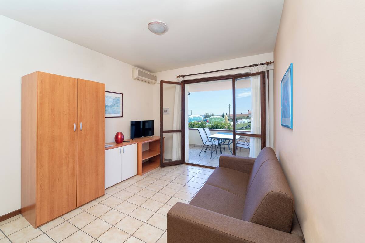 A modern living room with a sofa, a TV, a wooden wardrobe, and a balcony with a table and chairs.