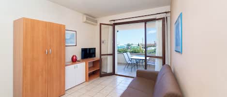 Ein modernes Wohnzimmer mit Sofa, Fernseher, einem Holzschrank und einem Balkon mit Tisch und Stühlen.