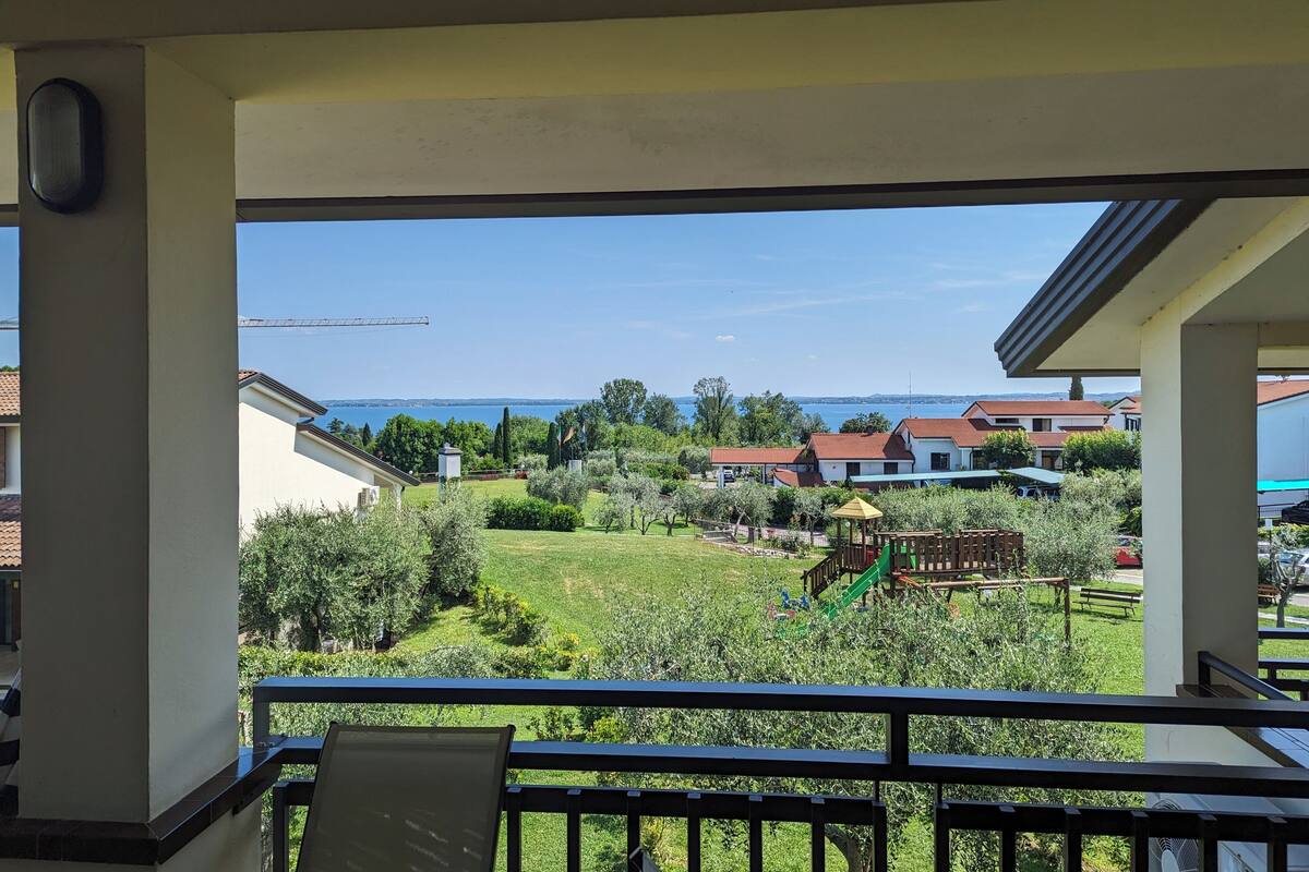 A balcony with a view of a residential area, a playground, and a body of water.