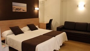 A hotel room with two beds, a sofa, a desk, and a wall-mounted picture. - Hostal Rocamar (Santander)