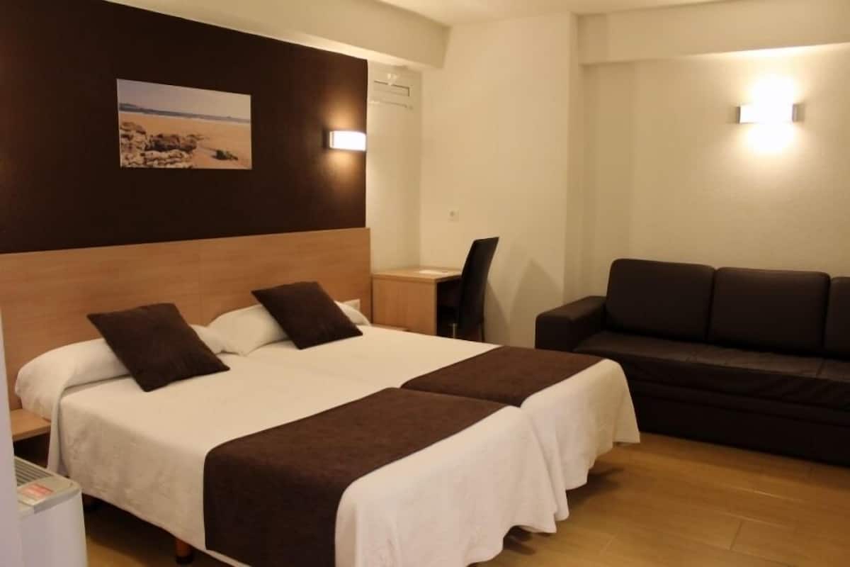 A hotel room with two beds, a sofa, a desk, and a wall-mounted picture.