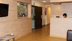 A reception area with a wooden reception desk, a flat-screen TV mounted on the wall, and a fire extinguisher on the wall. - Hostal Rocamar (Santander)