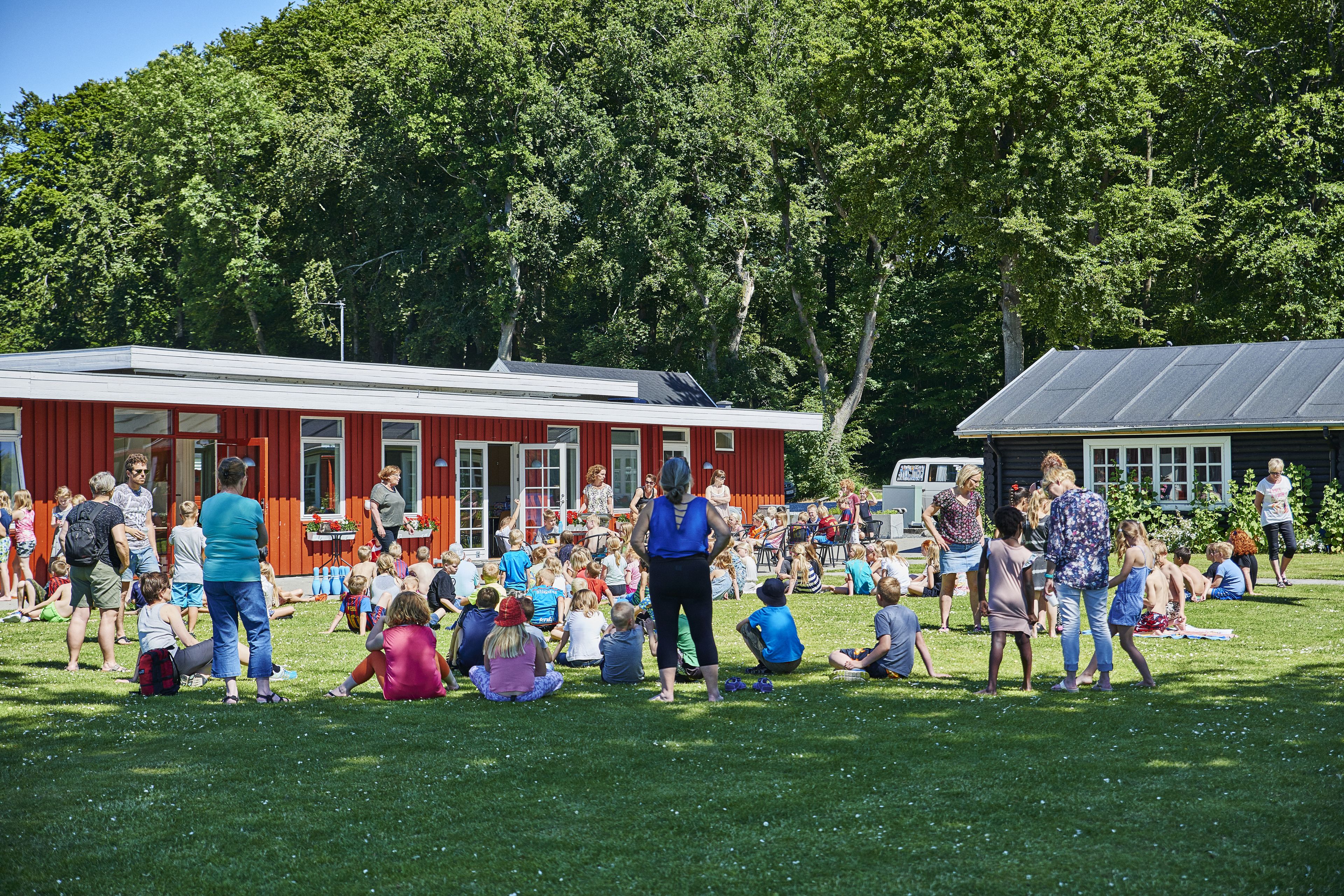 A group of people gathered outdoors in a grassy area with a red building in the background.