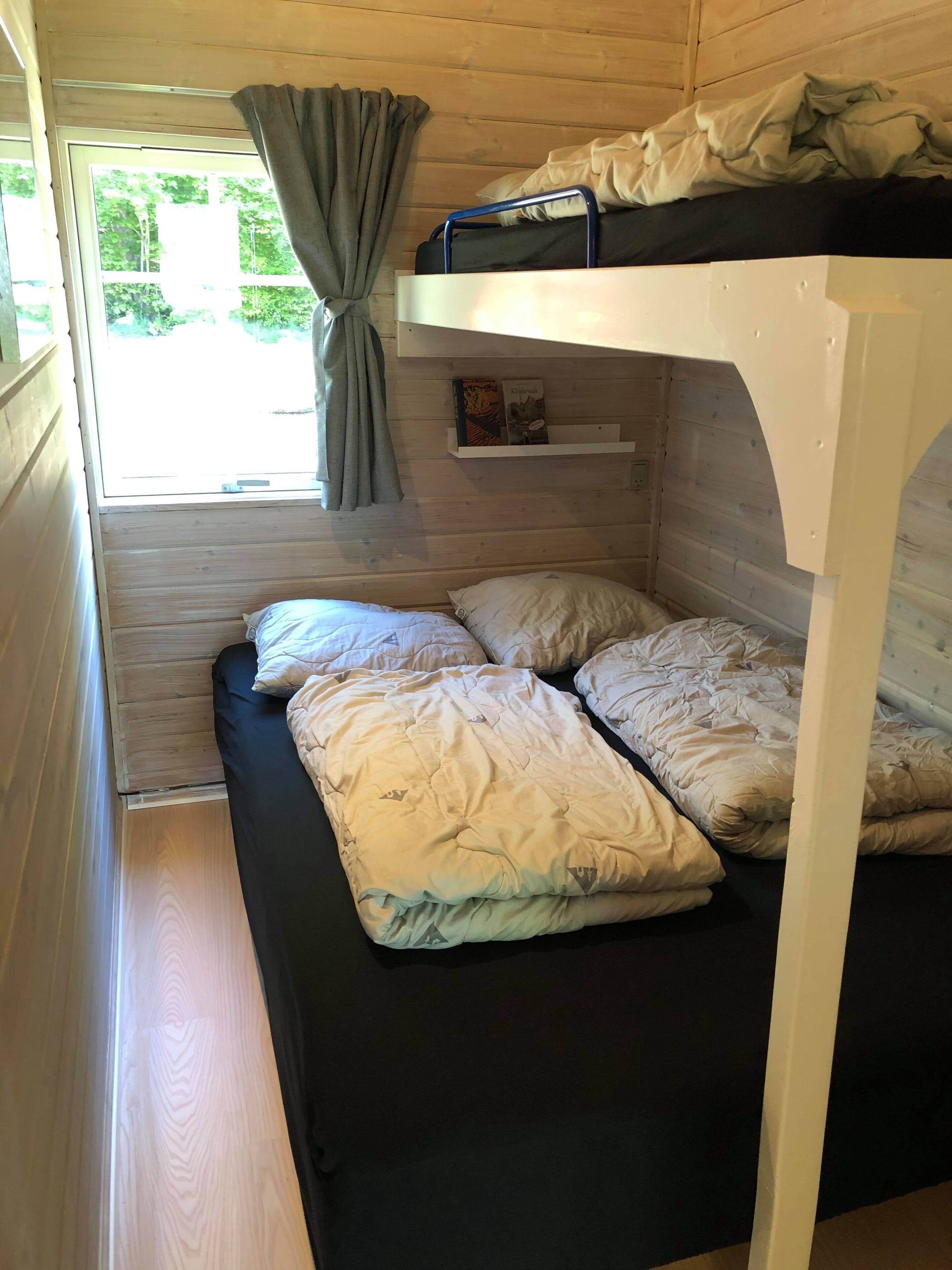 Habitación con literas, ventana, cortinas y estante con libros.