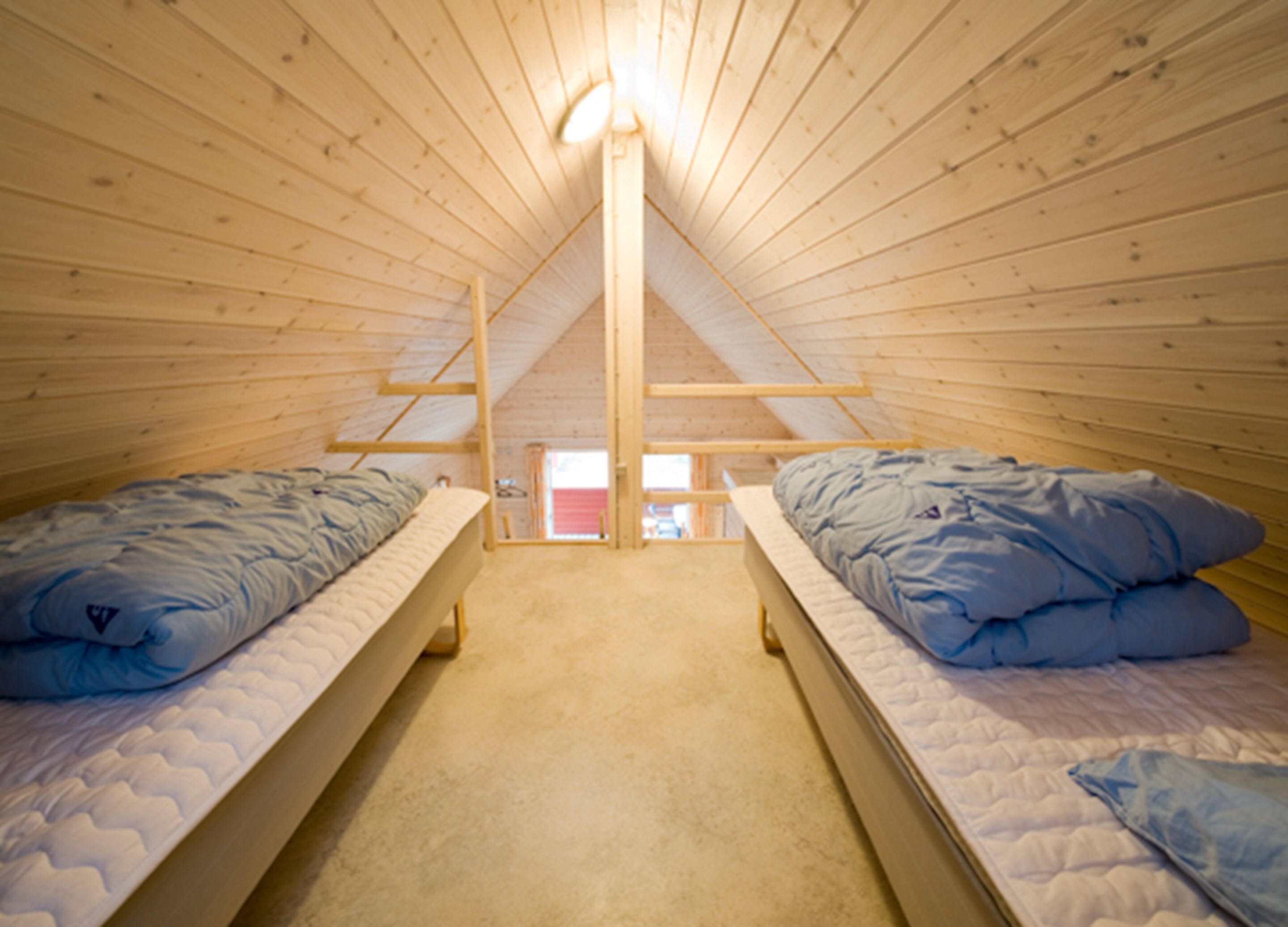 A small attic bedroom with two single beds, wooden ceiling beams, and a sloped roof.
