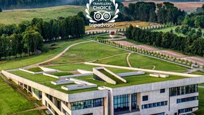 Een modern gebouw met een plat dak en grote ramen, omgeven door groene velden en bomen.