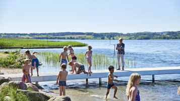 Un groupe de personnes se trouve dans une zone de baignade au bord d’un lac, avec une jetée et une personne qui s’y tient debout.