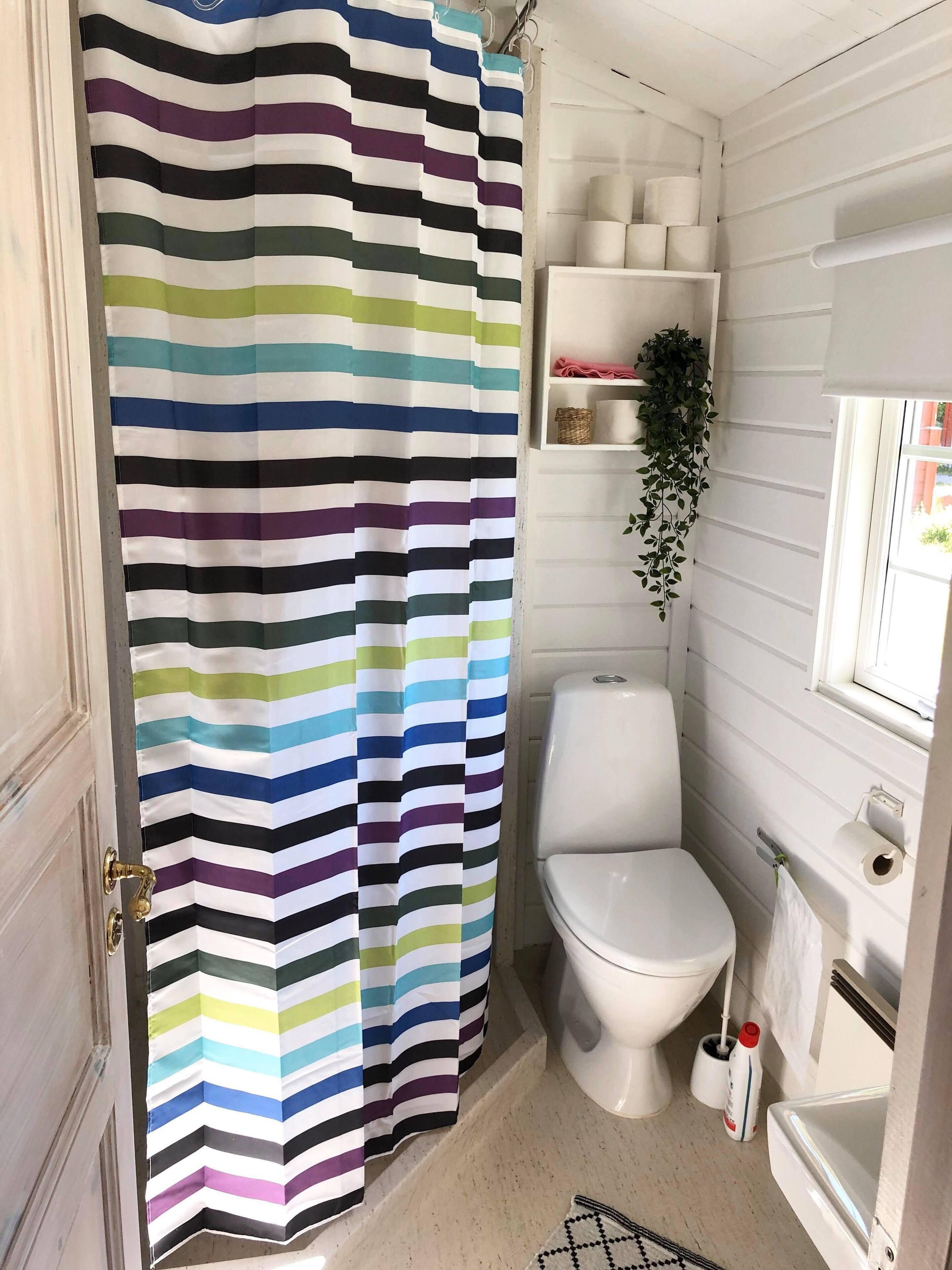 A bathroom with a striped shower curtain, a toilet, a shelf with toiletries, and a hanging plant.