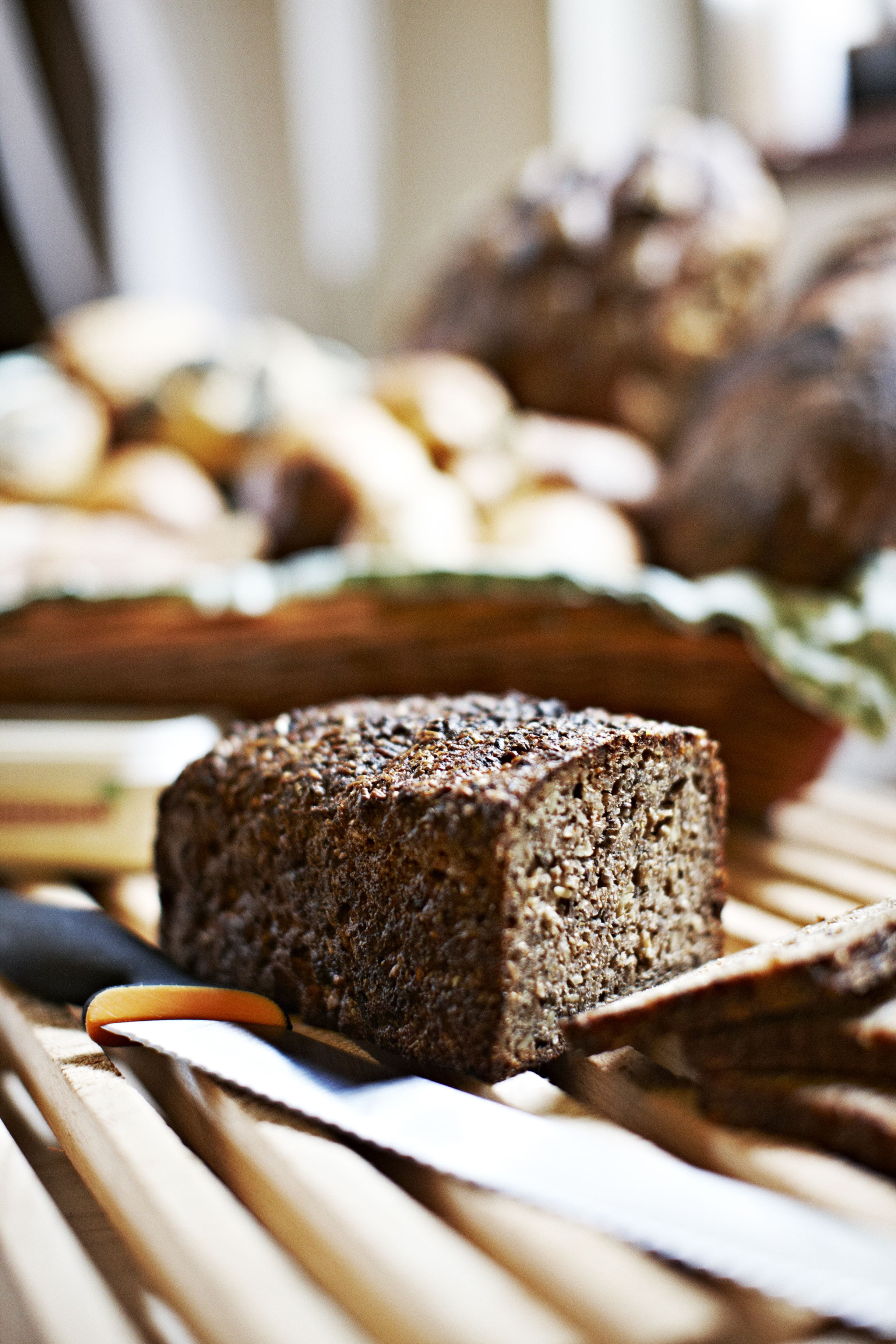 A loaf of dark rye bread on a wooden surface with a knife and a piece of bread.
