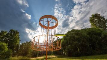 A disc golf basket in a park with trees and grass.