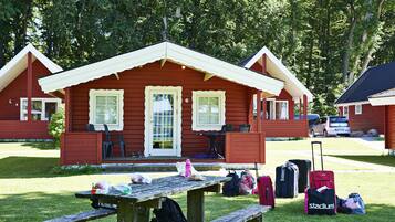 Une cabane rouge avec deux fenêtres et une porte, entourée de bagages et d’une table de pique-nique.