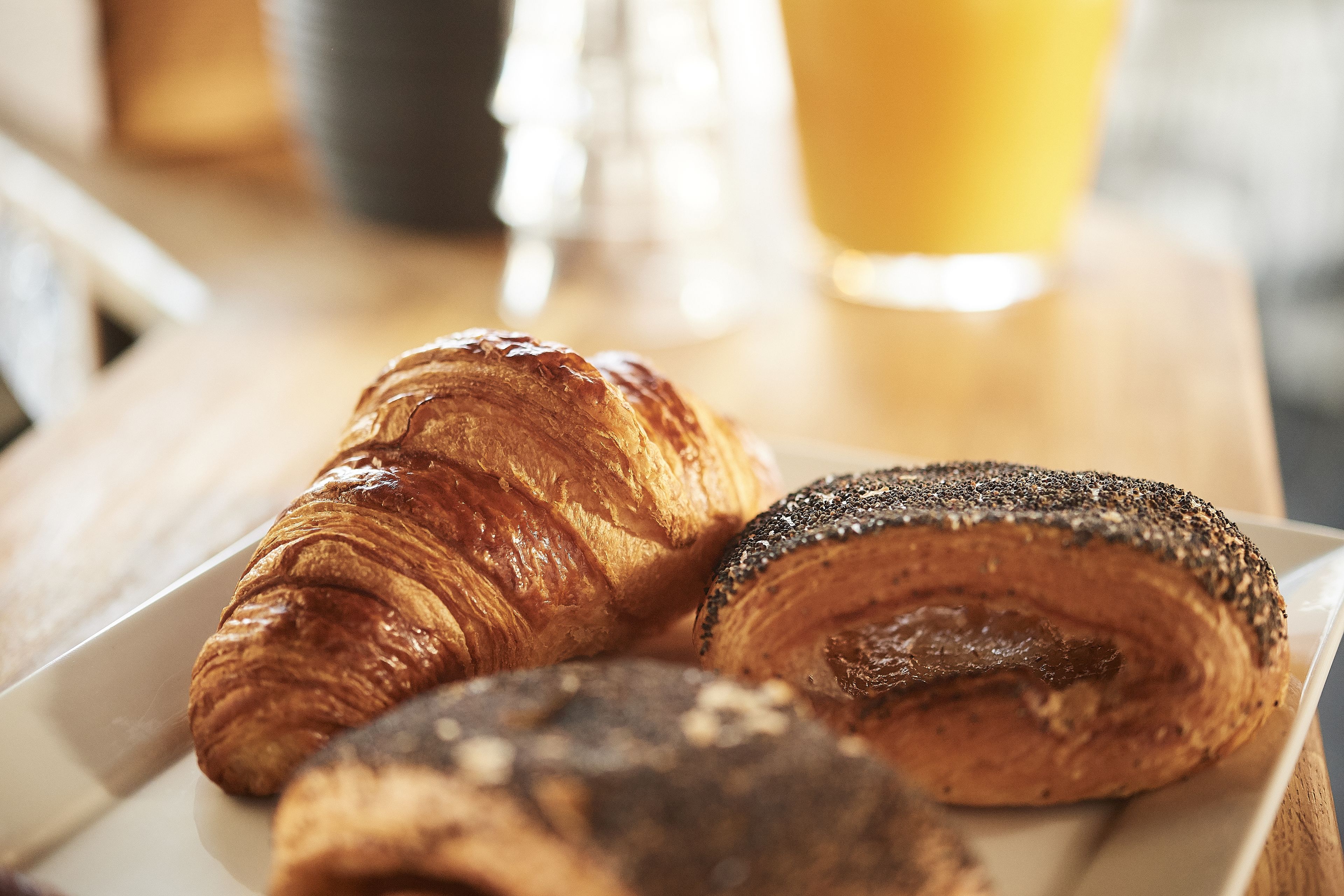 A plate with three pastries, a glass of orange juice, and a salt shaker on a wooden table.