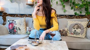 A woman sitting on a sofa with a dog pillow and a vintage-style pillow, a bowl, and a wine glass on a table. - Sky Kamer Hotel (Antalya)