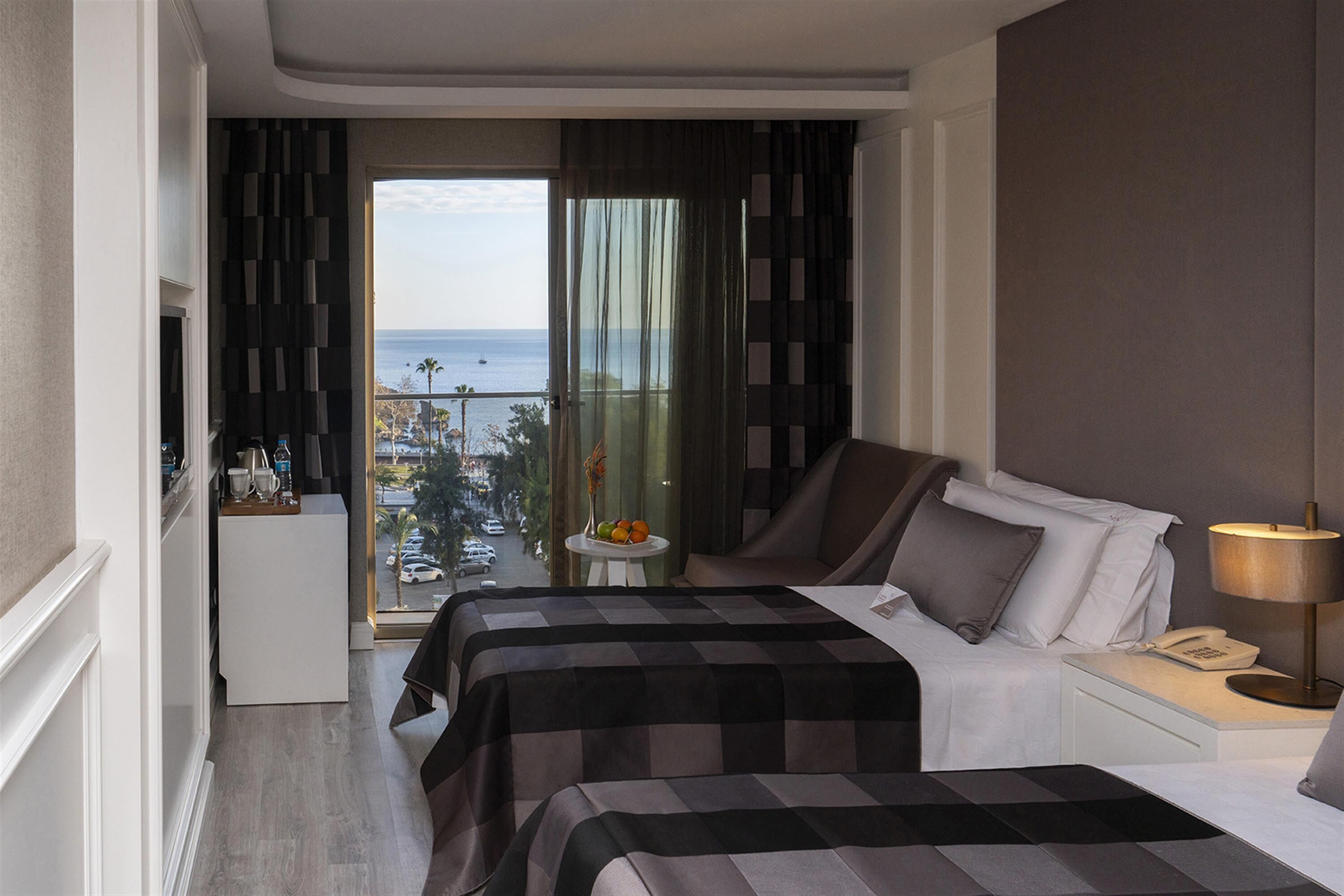 A hotel room with two beds, a small table with fruit, a view of the sea, and a balcony.