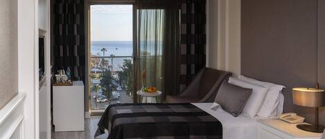 A hotel room with two beds, a small table with fruit, a view of the sea, and a balcony.