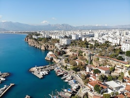 Un paysage urbain côtier avec un port de plaisance, des bâtiments et des montagnes en arrière-plan.
