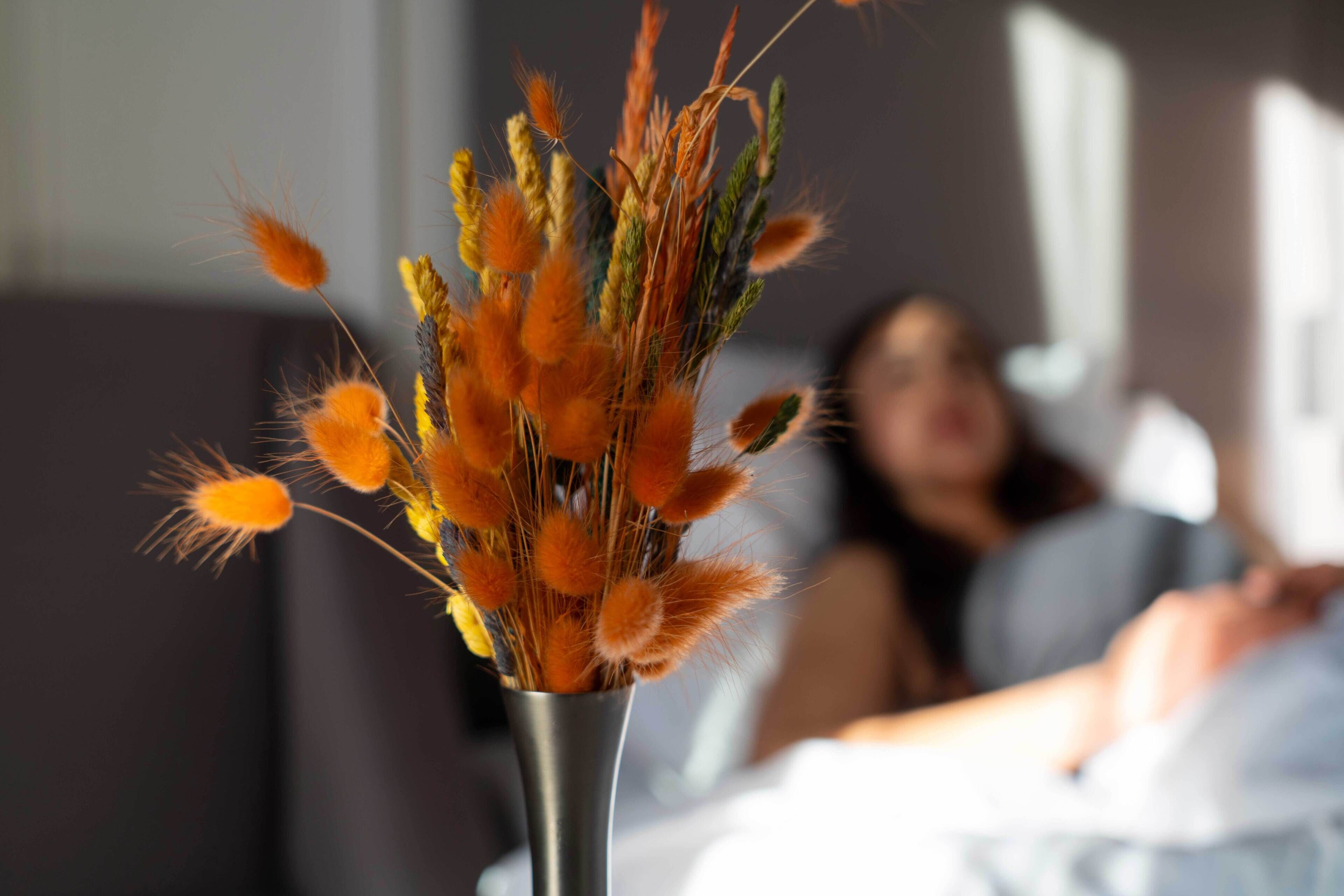 A vase with dried orange and yellow flowers on a bedside table in a hotel room.