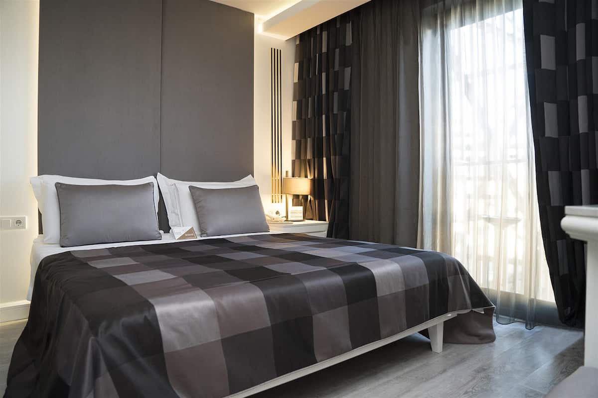 Une chambre d’hôtel moderne avec un grand lit, une table de chevet avec une lampe et une vue sur la ville par la fenêtre.