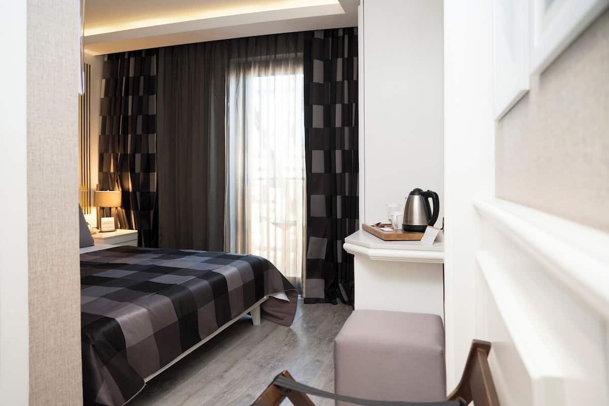 Une chambre d’hôtel avec un lit, un bureau doté d’une bouilloire, une chaise et une fenêtre avec des rideaux.