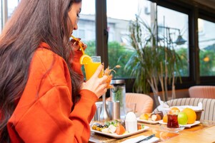 Una persona sentada a una mesa, comiendo y tomando algo, con una vista a la ventana de fondo.