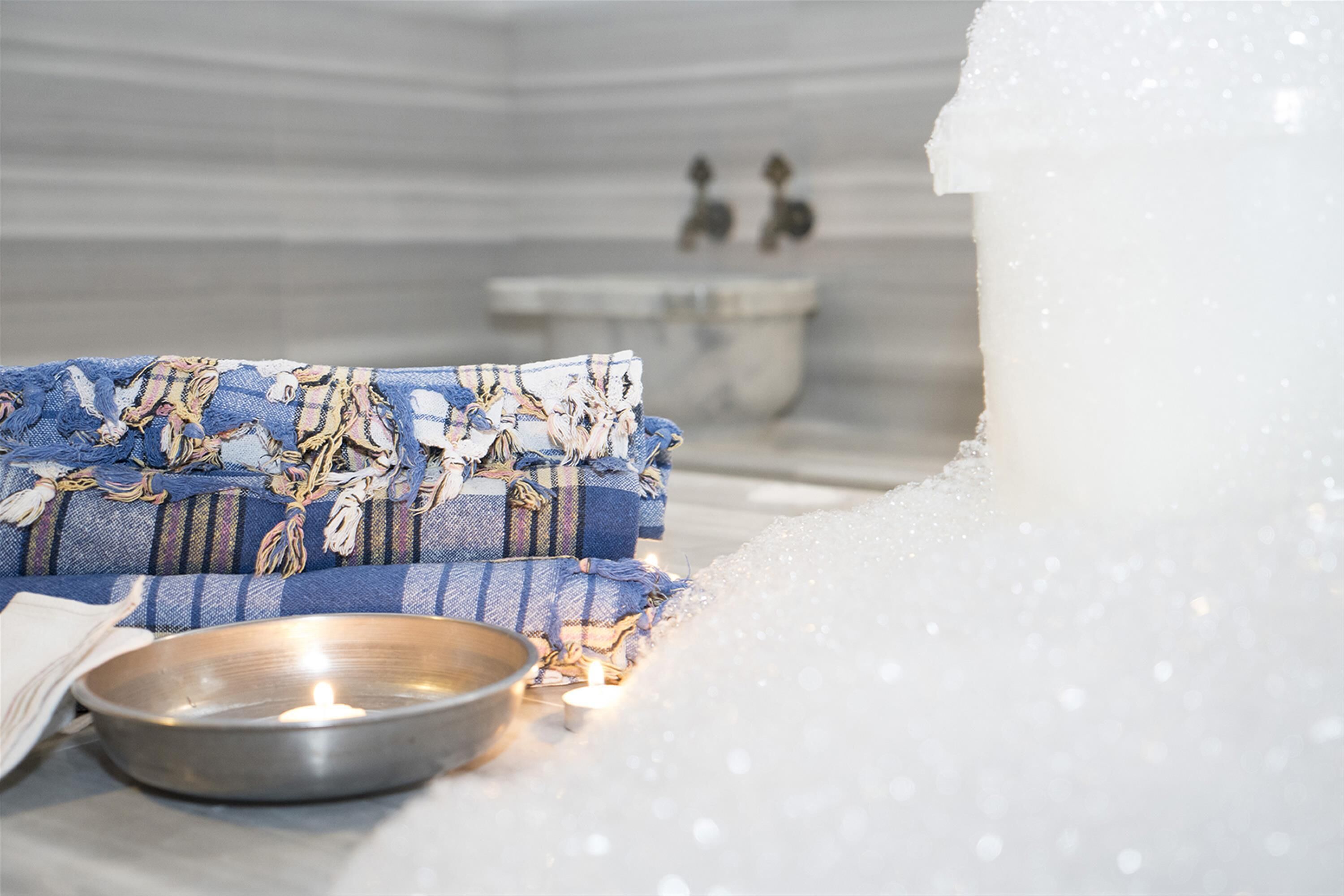 A spa room with a stone bench, a metal bowl, and a candle.