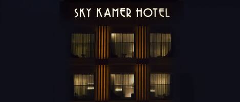 Exterior del hotel Sky Kamar de noche, con una fachada moderna de líneas verticales e iluminación de señalización.