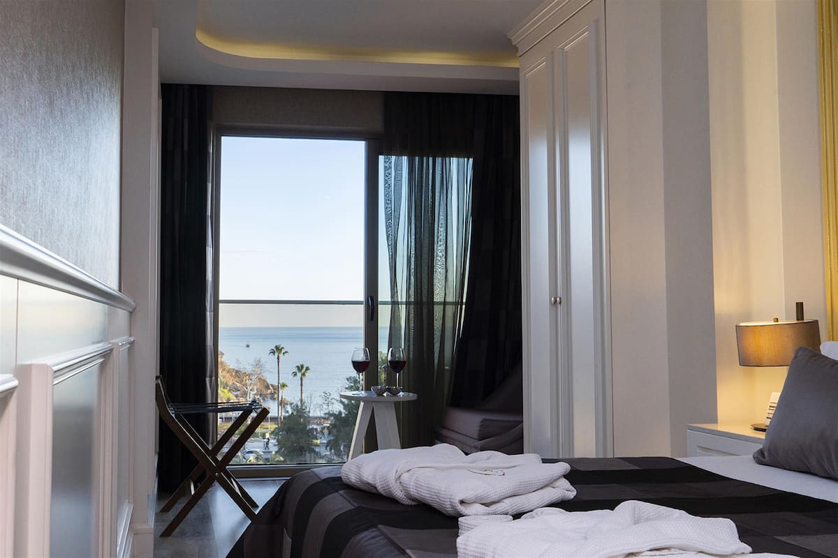 Une chambre d’hôtel avec un lit, une table de chevet, une lampe, une fenêtre avec des rideaux et une vue sur la mer.