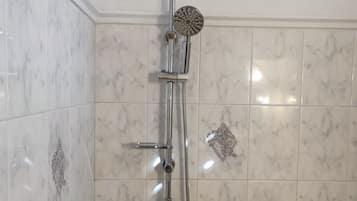 A bathroom with a shower, toilet, and a marble-tiled wall.