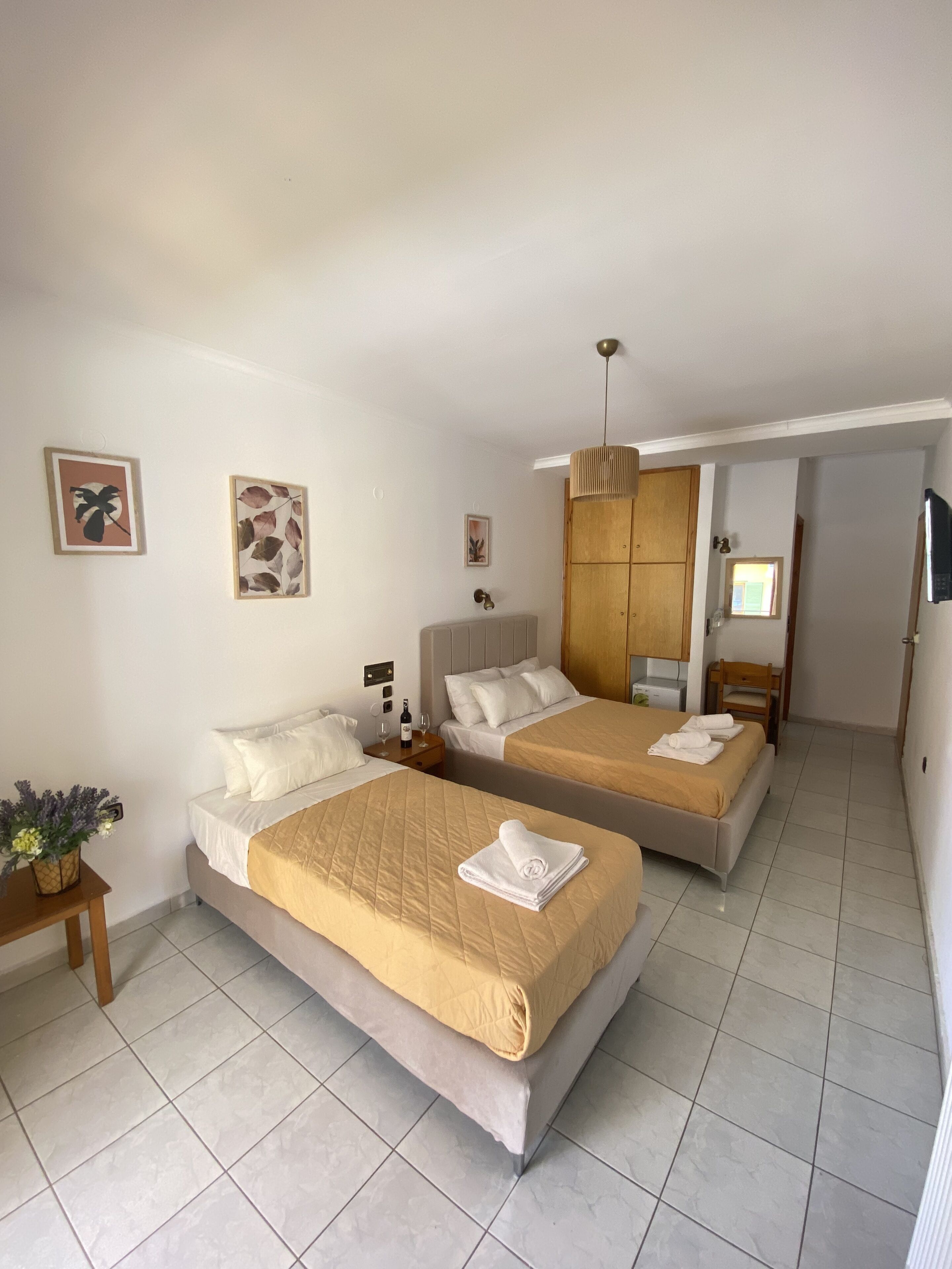 Een hotelkamer met twee bedden, een houten garderobe, een kleine tafel met een vaas en een televisie aan de muur.