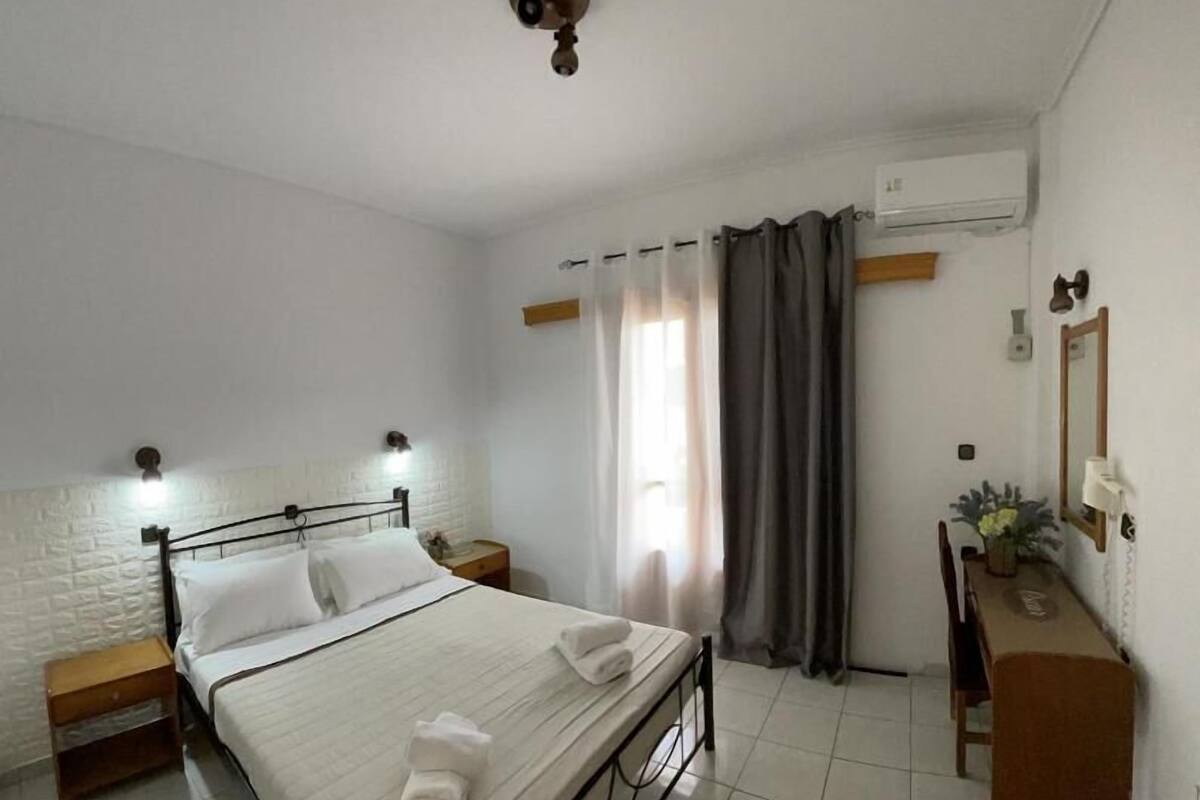 Un dormitorio limpio y bien iluminado, con cama, mesitas de noche, cómoda y espejo.
