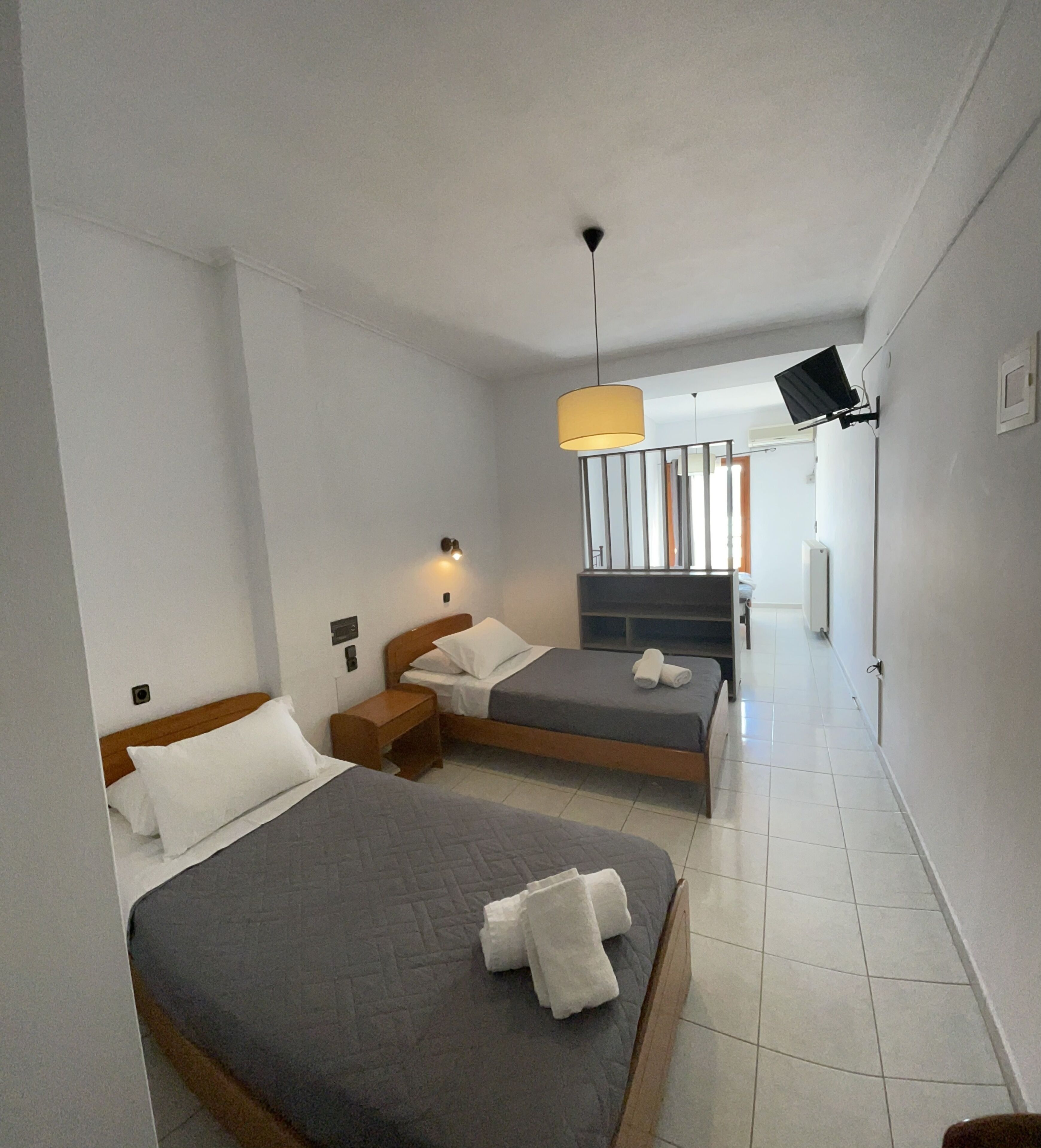 Ein Hotelzimmer mit zwei Betten, einem kleinen Tisch, einer Lampe und einem an der Wand montierten Fernseher.