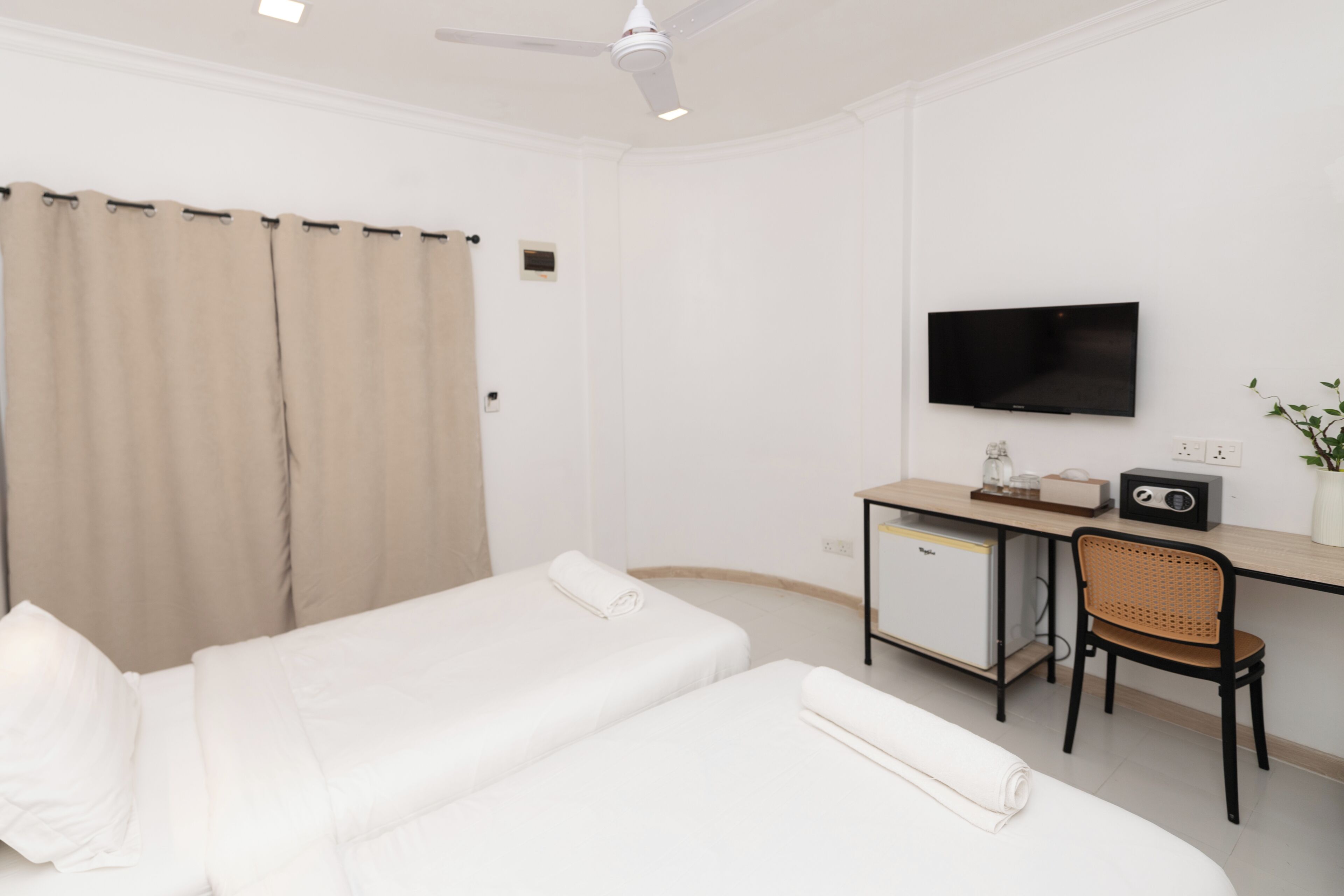 A hotel room with two beds, a desk, a chair, a television, and a small refrigerator.