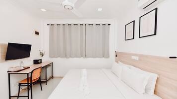 Habitación de hotel con cama, escritorio con silla, televisor y ventilador de techo.
